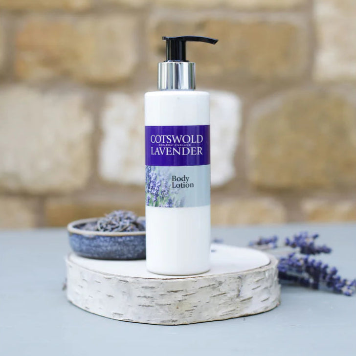 Body lotion bottle with Coisswold Lavender label on a stone surface with lavender flowers.