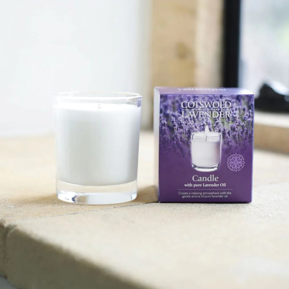 Candle in a glass holder next to its packaging on a wooden surface