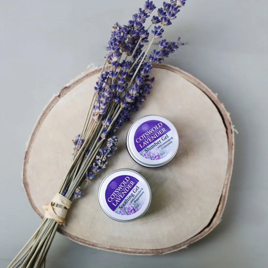Three tins of Cotswold Lavender Cream on a wooden board with lavender flowers.