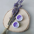 Three tins of Cotswold Lavender Cream on a wooden board with lavender flowers.